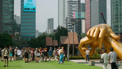 Crowds-of-Foreigner-Tourists-Travelers-Take-Pictures-with-Famous-Gangnam-Style-Hand-Sculpture-by-Coex-in-Seoul-Downtown-of-Gangnam-with-Office-Skyscrapers-in-Backdrop