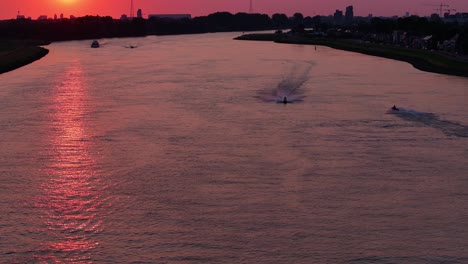 Jet-ski-riders-speeding-along-a-river-under-the-red-sunset-of-a-Rotterdam-night