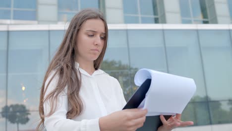 Young-entrepreneur-woman-looking-paper-documents-near-office,-close-up