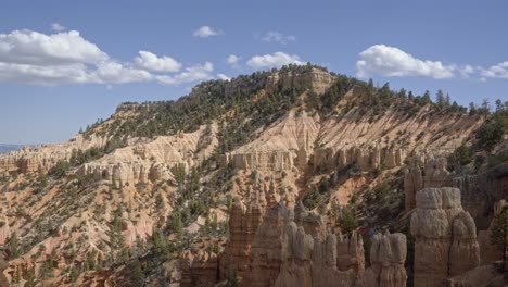Eine-Nach-Oben-Geneigte-Aufnahme-Zeigt-An-Einem-Warmen,-Sonnigen-Sommertag-Einen-Großen-Orangefarbenen-Sandsteinberg,-Umgeben-Von-Hoodoo-Formationen-Und-Kiefern-In-Der-Wüste-Im-Süden-Utahs