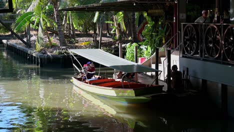 Der-Bootsmann-Sitzt-An-Der-Treppe-Und-Wartet-Auf-Seine-Passagiere,-Die-In-Einem-Der-Beliebtesten-Geschäfte-Auf-Dem-Schwimmenden-Markt-Damnoen-Saduak-In-Thailand-Souvenirs-Kaufen