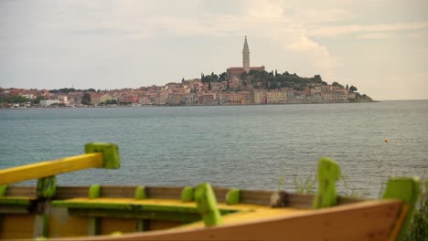 Young-woman-walks-past-boat-looking-out-to-the-city-of-Rovinj,-Croatia