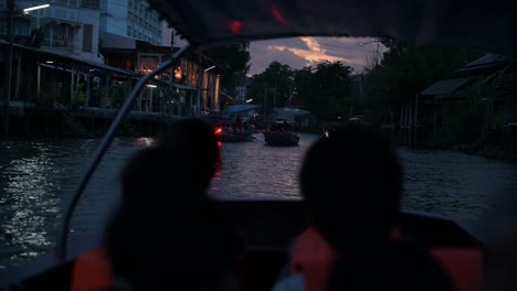 A-wooden-tour-boat-moving-towards-the-river-to-where-the-sun-was-setting-while-the-rest-of-the-boats-are-going-back-into-the-canal-of-Amphawa-Floating-Market,-Thailand