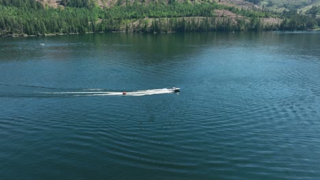 Drone-shot-of-a-motorboat-pulling-people-behind-it-on-Spirit-Lake,-Idaho