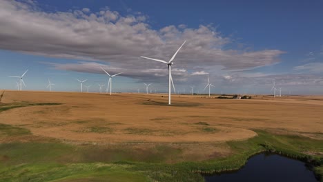 A-drone-flies-up-and-across-a-prairie-farmland-wind-farm-as-windmills-spin-in-southern-Alberta,-Canada