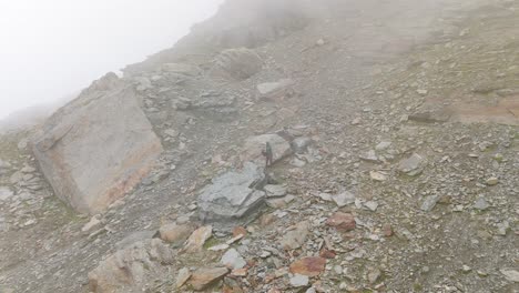 Aerial-View-Of-Lone-Hiker-Standing-On-Rocky-Mountain-Hillside-In-Dense-Hazy-Fog