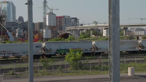 Montreal-Réseau-Express-Métropolitain-REM-Train-Running-on-a-Elevated-Line-in-Front-of-the-Skyline-and-Stopped-Freight-Trains-During-Golden-Hour