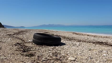 Tire-and-plastics-on-beach,-pollution-of-seaside-on-Mediterranean-coastline,-environment-disaster-of-garbage-thrown-on-shoreline