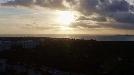 Slow-right-trucking-aerial-drone-shot-of-a-stunning-yellow-golden-ocean-sunset-with-tropical-greenery-below-from-Crandon-Park-in-Key-Biscayne-outside-of-Miami,-Florida-on-a-warm-sunny-summer-evening