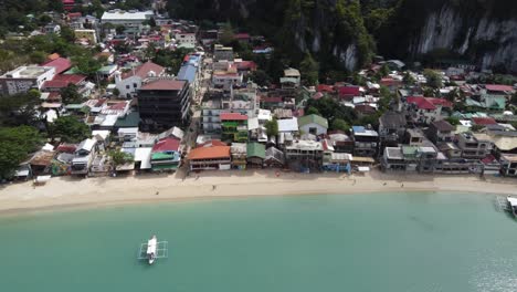 Small-tropical-island-of-El-Nido-town-and-rooftops,-a-beachfront-port-in-Bacuit-Bay,-Philippines,-Drone-shot