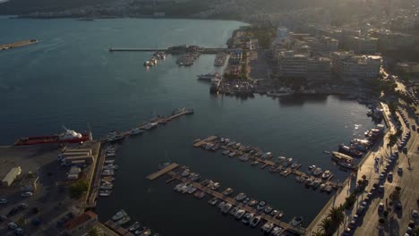 Aerial-of-cityscape-with-busy-road-and-boats-docked-on-the-port-at-sunset-in-Greece