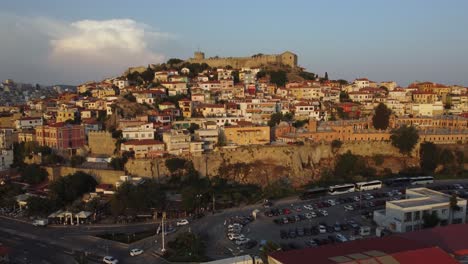 Aerial-pull-back-and-reveal-of-hill-hill-with-ancient-fortress-in-Kavala,-Greece-at-sunset