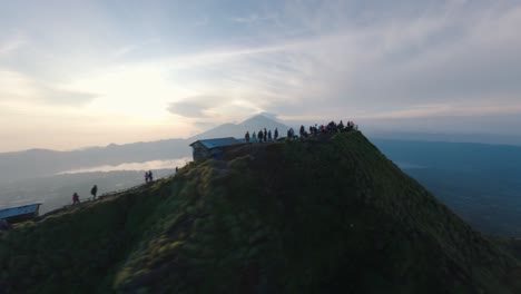 Drone-flying-around-crowd,-Mount-Batur-in-Bali,-beautiful-sunrise,-hiking-group,-sunflares-in-people-silhouettes,-epic-aerial-view-of-volcano-peak,-morning-in-Indonesia,-sun-rise-hike-on-mount-Batur