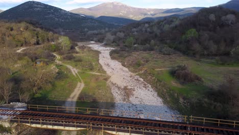 Aerial-ascend-over-abandoned-train-tracks-on-dried-up-riverbed-surrounded-by-mountains