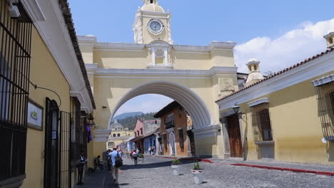 Tourists-walk-cobble-street-below-Santa-Catalina-Arch-in-Antigua,-GTM