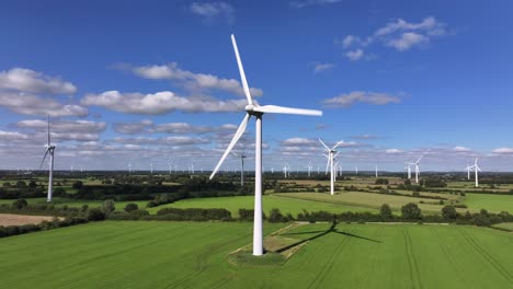 Wind-turbines-farming-wind-energy,-green-fields,-blue-sky,-countryside,-sunny,-slow-drone-orbit,-slow-shutter-speed