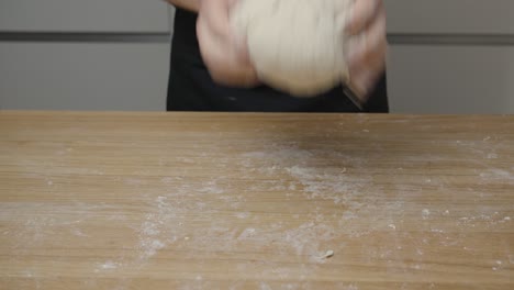 Man-kneading-a-ball-of-pizza-dough-with-his-hands-on-a-kitchen-shelf