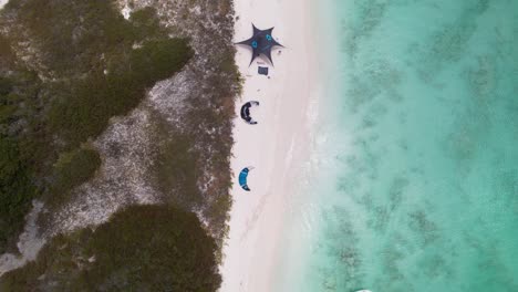 Birdseye-view-of-Kites,-camp-awnings-and-surfers-at-Crasqui-Island,-Los-Roques