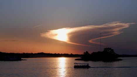 Pontoon-boat-motors-through-sunset-sun-beam-on-golden-lake-water