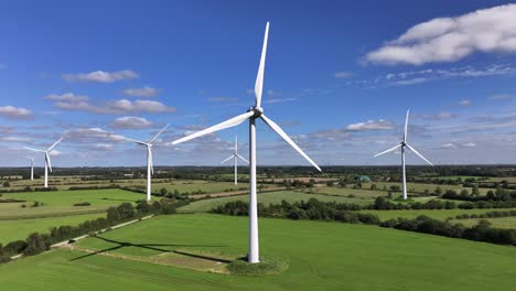 Wind-turbines-farming-wind-energy,-green-fields,-blue-sky,-countryside,-sunny,-static-drone-shot,-symbolic,-picturesque