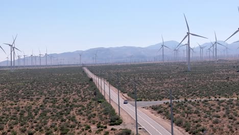 Truck-driving-across-a-desert-road-in-middle-of-wind-turbines,-in-sunny-Mojave,-USA---Ascending,-aerial-view