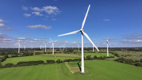 Wind-turbines-farming-wind-energy,-green-fields,-blue-sky,-countryside,-sunny,-static-drone-shot,-slow-shutter