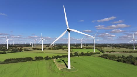 Wind-turbines-farming-wind-energy,-green-fields,-blue-sky,-countryside,-sunny,-slow-drone-orbit,-green-sustainable-power