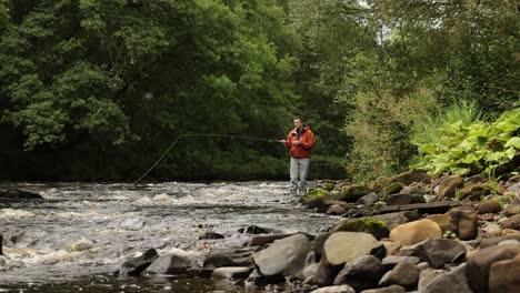 Low-angle-shot-of-a-flyfisherman-casting-and-walking-down-a-riverbank