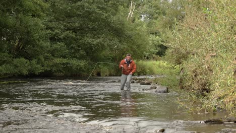 Hand-held-shot-of-a-flyfisherman-wading-down-the-river-and-casting