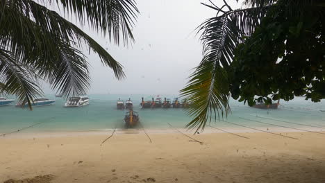 Rainy-monsoon-day-in-Phi-Phi-Islands-thailand,-empty-beach-with-tied-down-longtail-and-yacht-boats
