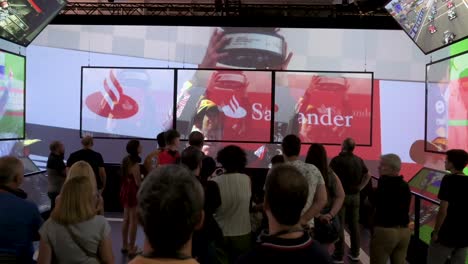 Während-Der-Ersten-Offiziellen-Formel-1-Ausstellung-Der-Welt-Auf-Der-Ifema-In-Madrid,-Spanien,-Sehen-Sich-Menschen-Ein-Montagevideo-Mit-Den-Gewinnern-Und-Feierlichkeiten-Des-F1-Grand-Prix-In-Der-Geschichte-Des-Sports-An