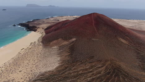 La-Graciosa-island:-aerial-view-traveling-in-to-the-Bermeja-mountain-and-Las-Conchas-beach-on-a-sunny-day-and-turquoise-waters
