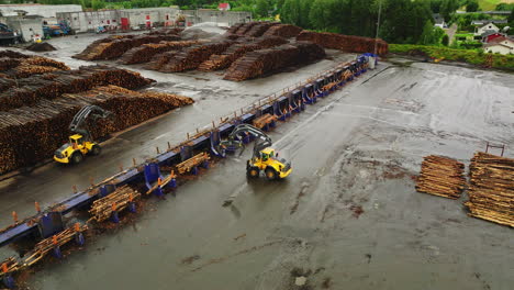 Log-loaders-in-Braskereidfoss-move-among-massive-piles-of-timber-logs,-aerial