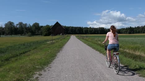 Woman-bicycling-country-road-in-countryside-in-summer