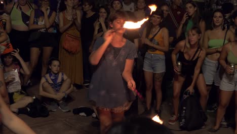 woman-performs-with-fire-poi-swinging-during-public-event,-women-and-children-watch-gathered-in-a-circle