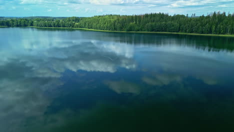 Aerial-drone-forward-moving-shot-over-lake-water-surface-with-clouds-in-sky-reflecting-in-water-surface
