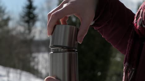 Woman-hands-opening-thermos-and-drinking-hot-drink-in-winter-forest-outdoors