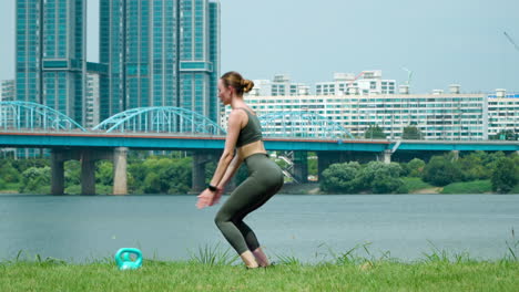 Fit-Fitness-Frau,-Die-An-Einem-Sommertag-Im-Han-River-Seoul-City-Park-Zweibeinige-Squat-Jump-Übungen-Durchführt