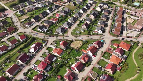 Residential-area,-uniform-single-family-houses-with-green-gardens-in-a-small-town,-sunny-day,-drone
