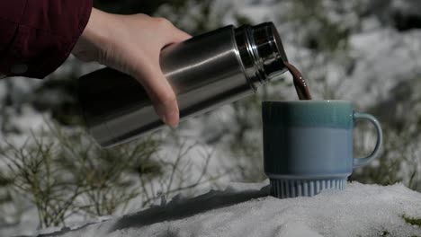 Hot-chocolate-pouring-into-mug-snowy-winter-forest,-hot-cocoa-cup-in-snow