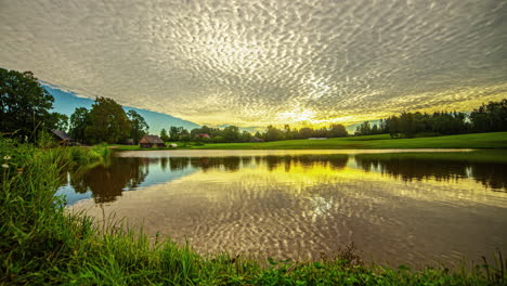 Golden-Sunlight-And-Cloudscape-Reflected-Over-Still-Water-Surface-Of-A-Lake-During-Sunrise