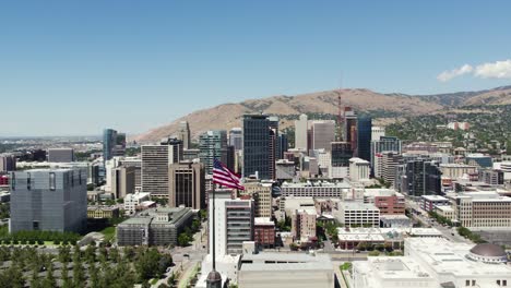 American-Flag-Waving-with-Downtown-Salt-Lake-City-Skyline,-Aerial-Orbit