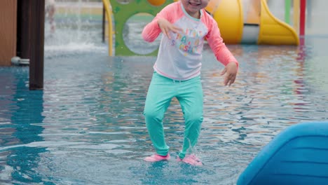 Excited-Little-Girl-Splashing-Water-With-Hands-and-Jumps-Playing-at-Outdoor-Water-Playground-During-Summer-Holidays