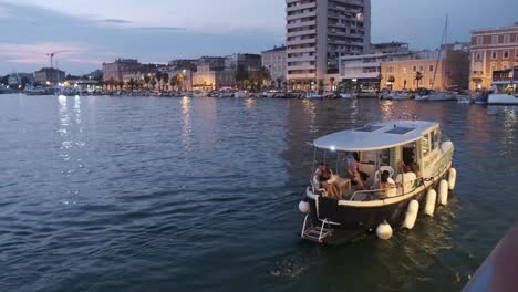 Night-sail-in-a-small-boat-in-Zadar-with-city-buildings-and-lights-reflecting-on-a-calm-sea-surface