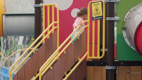 Three-years-old-girl-with-pigtails-walking-up-the-stairs-to-ride-slide-at-water-park