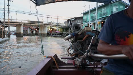 Guiding-his-wooden-boat-along-the-waterways-of-Amphawa-Floating-Market,-the-boatman-is-carrying-his-passengers-of-tourists-on-a-night-tour-in-Samut-Songkhram,-Thailand