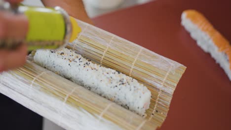 A-professional-chef-adds-seeds-to-a-roll-of-rice,-preparing-a-sushi-dish,-traditional-Japanese-cuisine