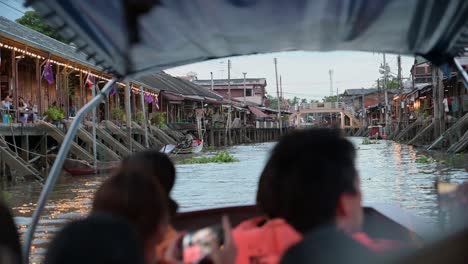 At-almost-sunset,-a-group-of-local-and-foreign-tourist-are-taking-a-tour-of-Amphawa-Floating-Market-while-cruising-on-a-wooden-boat,-at-Samut-Songkhram,-Thailand