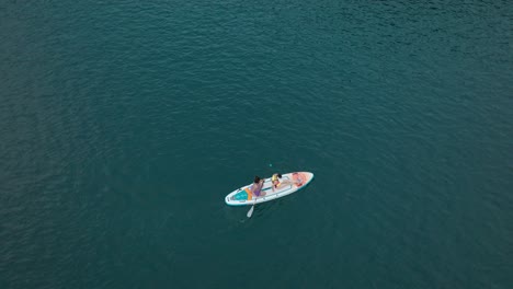 Two-girls-paddling-on-colorful-SUP-board-over-deep-blue-water-lake