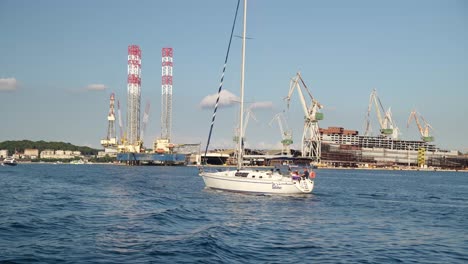 Yacht-and-crew-sail-past-oil-platform-at-the-shipyard-Uljanik-in-Pula,-Croatia